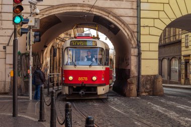 Klasik kırmızı Prag tramvayı şehir merkezinde ikonik şehir taşımacılığı ve mimari sergilenen tarihi bir taş kemer yolundan doğuyor. Prag, Çek Cumhuriyeti - 24 Şubat 2025.