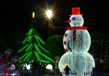 Madrid, İspanya 1 Aralık 2022 'de eşarplı ve kırmızı şapkalı bir kardan adam Noel ağacının yanında. Noel ışıklarının gece fotoğrafı.