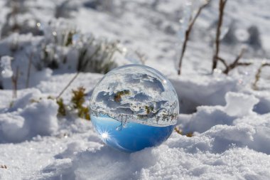 Reflection in a crystal ball of a mountain landscape with snow on a sunny day and blue sky. winter photo. Snow storm in the mountains. Mountains and pine trees covered with snow.