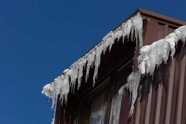 Ice icicles on the roofs of houses in winter. winter atmosphere. Consequences of the cold in the mountains. Frozen water.