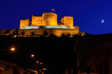 Consuegra kalesinin gece fotoğrafı. Ayla birlikte gece manzarası. Değirmenli ve şatolu tepe.