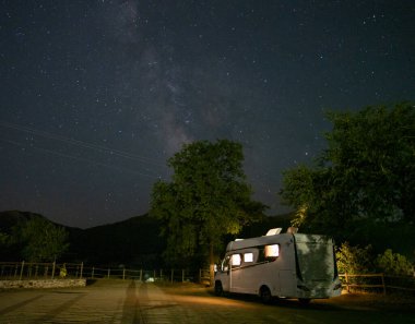Kırsalda yıldızların altında bir karavanın gece fotoğrafı. Samanyolu ile karavan. Motosiklet yolculuğu.