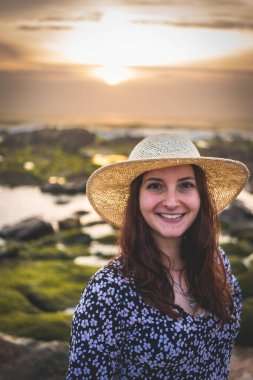 Şapkalı kadın Gaia, Porto, Portekiz 'deki Rocky Beach' te günbatımının tadını çıkarıyor. Juni 17 2023.