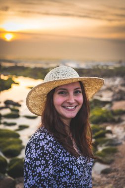 Şapkalı kadın Gaia, Porto, Portekiz 'deki Rocky Beach' te günbatımının tadını çıkarıyor. Juni 17 2023.