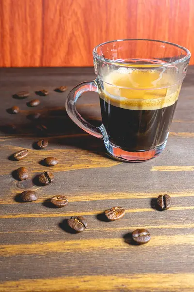Kahve çekirdekleri ile süslenmiş ahşap bir masanın üzerinde cam bir fincan Expresso..