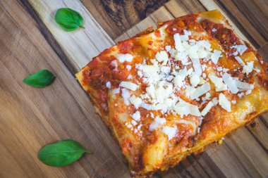 Ev yapımı lazanya, fesleğenle süslenmiş ahşap bir kesme tahtanın üstünde..