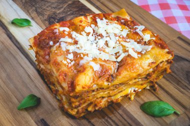 Ev yapımı lazanya, fesleğenle süslenmiş ahşap bir kesme tahtanın üstünde..