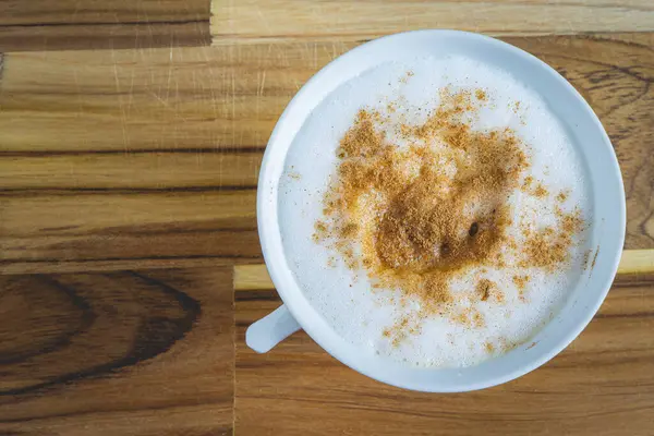 Lezzetli ev yapımı Cappuccino, beyaz bir fincanda, ahşap bir masada. Ev yapımı kahve..