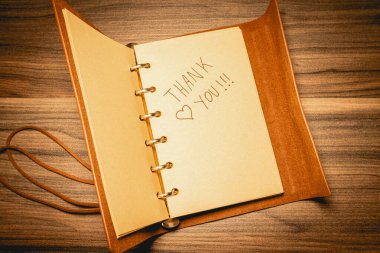 Deri bir defterde, ahşap bir arka planda bir teşekkür notu.