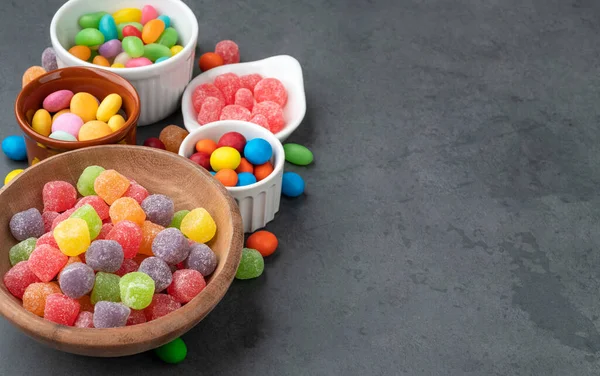 Assorted colorful candies in bowls over stone background with copy space.
