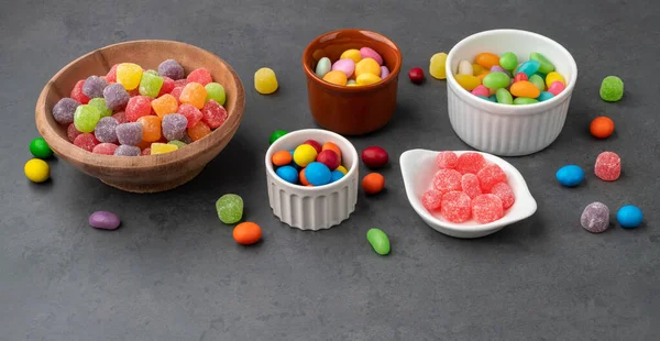 Assorted colorful candies in bowls over stone background.