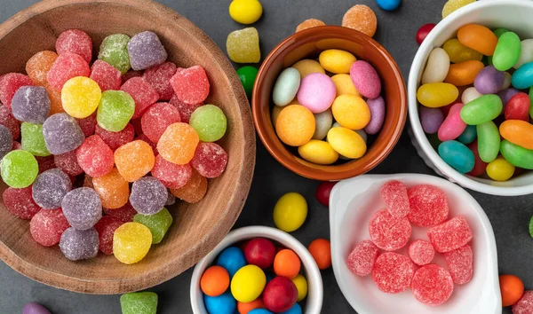 Assorted colorful candies in bowls over stone background.