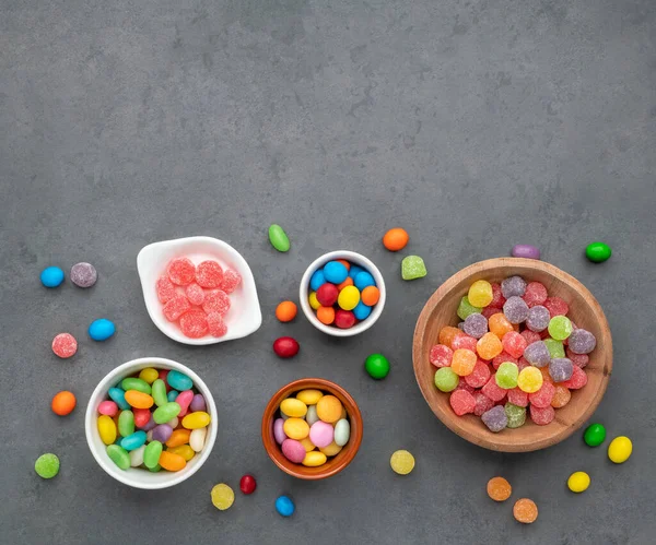Assorted colorful candies in bowls over stone background with copy space.
