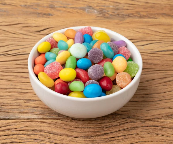 Assorted colorful candies in a bowl over wooden table.