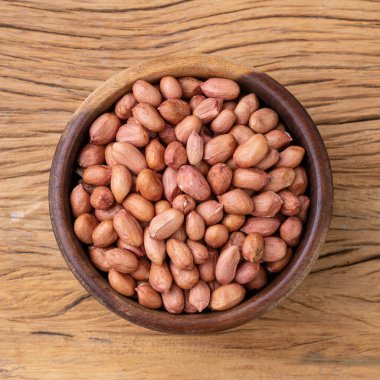 Raw peanuts in a bowl over wooden table.