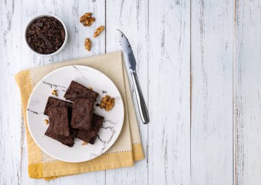 Brownies on a plate with chocolate pieces and walnuts over white wooden table with copy space.