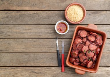 Grilled calabrese sausage portion with onion, farofa and pepper over wooden table with copy space.