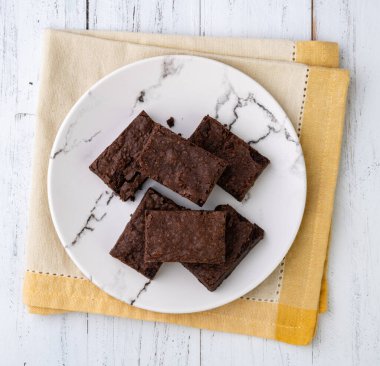 Brownies on a plate with chocolate pieces and walnuts over white wooden table.