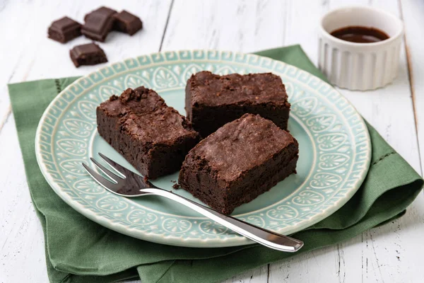 Brownies on a green plate with chocolate pieces and syrup over white wooden table.