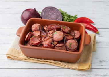 Grilled calabrese sausage slices with onion, pepper and herbs over white wooden table.