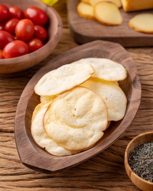 Çeri domatesli bir kasede füme peynirli cips ve ahşap masada kekik..
