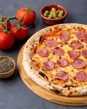 Calabrese sosis tarzı pizza. Arka planda domates, zeytin ve keklikotu var..