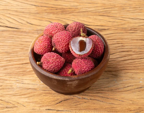 Lychees in a bowl with cut fruit over wooden table.