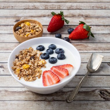 Çilekli yoğurt, yaban mersini ve tahıl gevreği ahşap bir masada..