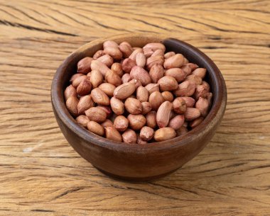 Raw peanuts in a bowl over wooden table.