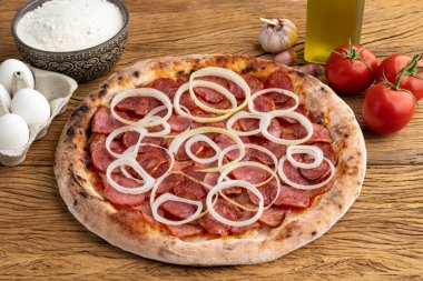 Soğan, domates, yumurta ve un ile ahşap masa üzerinde Calabrese sosis tarzı pizza..