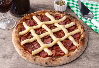 Calabrian sausage and Catupiry cream cheese style pizza over wooden table with wine, oregano and spatula. clipart