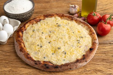 Dört peynirli pizza, domates, yumurta ve un, ahşap masanın üzerinde..