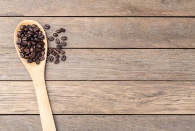 Kahve çekirdekleri bir kaşık üzerinde ahşap masada fotokopi alanı ile.