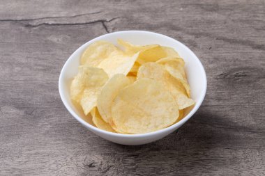 Tahta masanın üzerinde bir kasede patates cipsi.