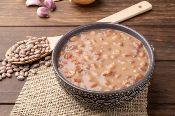 Tahta masanın üzerinde, soğan ve sarımsaklı bir kasede pişmiş kahverengi fasulye..