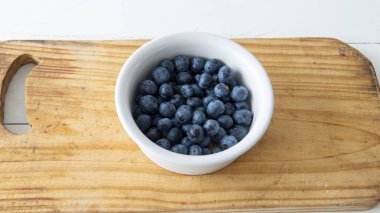 Taze yaban mersinleriyle dolu küçük beyaz bir seramik kasenin düz manzarası vardı. Tahta bir masanın üstüne yerleştirilmiş.