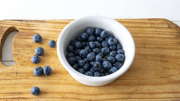 Taze yaban mersinleriyle dolu küçük beyaz bir seramik kasenin düz manzarası vardı. Tahta bir masanın üstüne yerleştirilmiş.