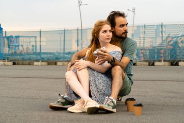 Genç çift kaykayda birlikte oturuyor ve gözlerini kaçırırken dışarıdan yemek yiyorlar. 