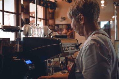 Meçhul, olgun bir kadının kahve malzemesi kullanarak içecek hazırladığını gördüm. Küçük kafede çalışan bir barista..