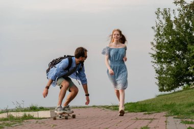 Olumlu genç adam, kız arkadaşı gri gökyüzüne doğru koşarken uzun tahtanın üstünde.