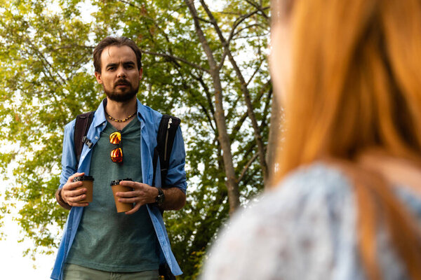 Serious young man with takeaway coffee standing against girlfriend 