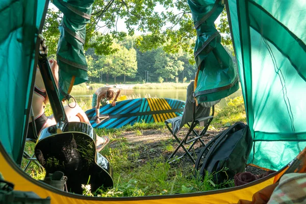 キャンプシーンのテントからの眺め 見知らぬカップルがスーパーボードに乗る準備をしている キャンプの一連のショット — ストック写真