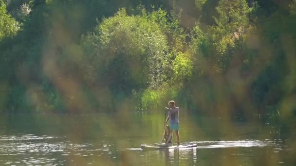 侧面看年轻的赤身裸体男子站在船舷上 与女友坐在他身后的漂浮在河边 透过草丛看 — 图库视频影像