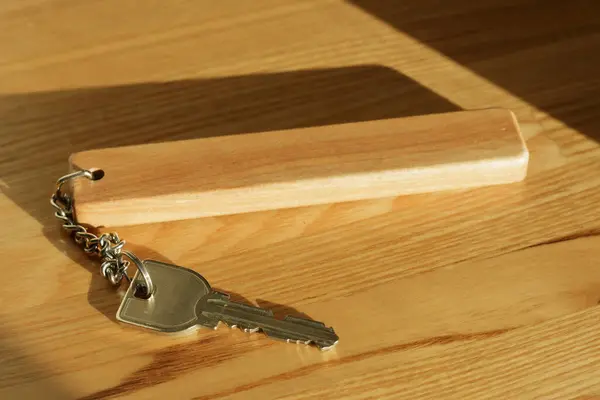 Silver coloured metal hotel room key attached to wooden key fob with chain