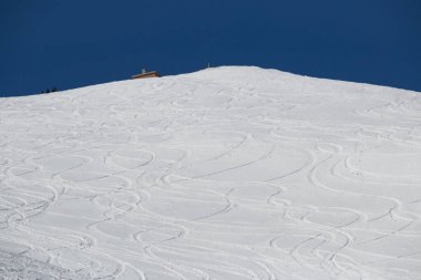 Mavi gökyüzünde Niseko dağı zirvesi. Kar üzerinde kayak ve snowboard izleri var.