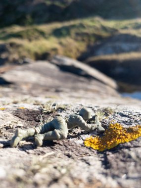 Plastik oyuncak asker kayaların üzerinde tüfeği doğrultarak yatıyor.