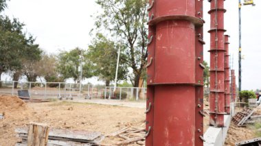 Metal fence post formwork. Closeup of concrete column formwork made of red painted steel on concrete base at fence construction site with copy space with selective focus.