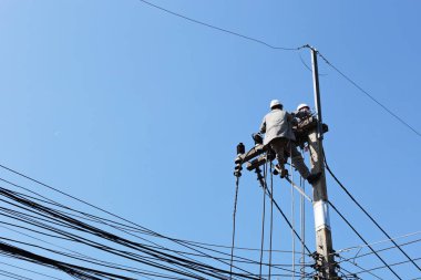 Electrician on the pole. Electricians are installing and maintaining high voltage transmission lines on pylons in urban area on bright blue sky background with copy space and selective focus.