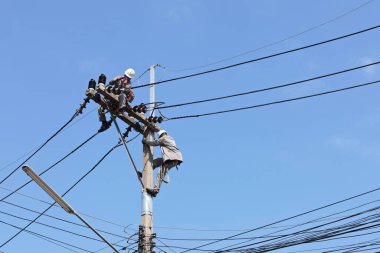 Electrician on the pole. Electricians are installing and maintaining high voltage transmission lines on pylons in urban area on bright blue sky background with copy space and selective focus.
