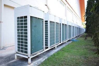 Air conditioner condenser behind the building. Row of condenser units of air conditioners for large buildings mounted on outdoor concrete floor with copy space and selective focus.